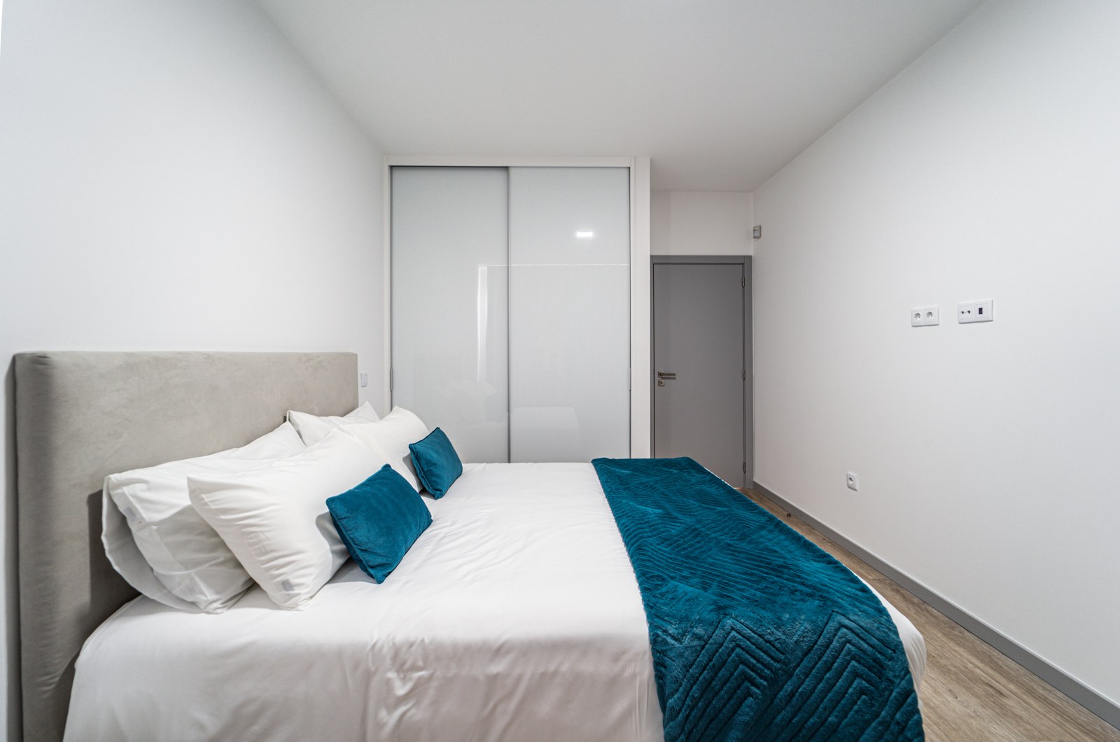 Bedroom with king bed, teal throw and built-in wardrobe at Guesthouse Olival, Gaula