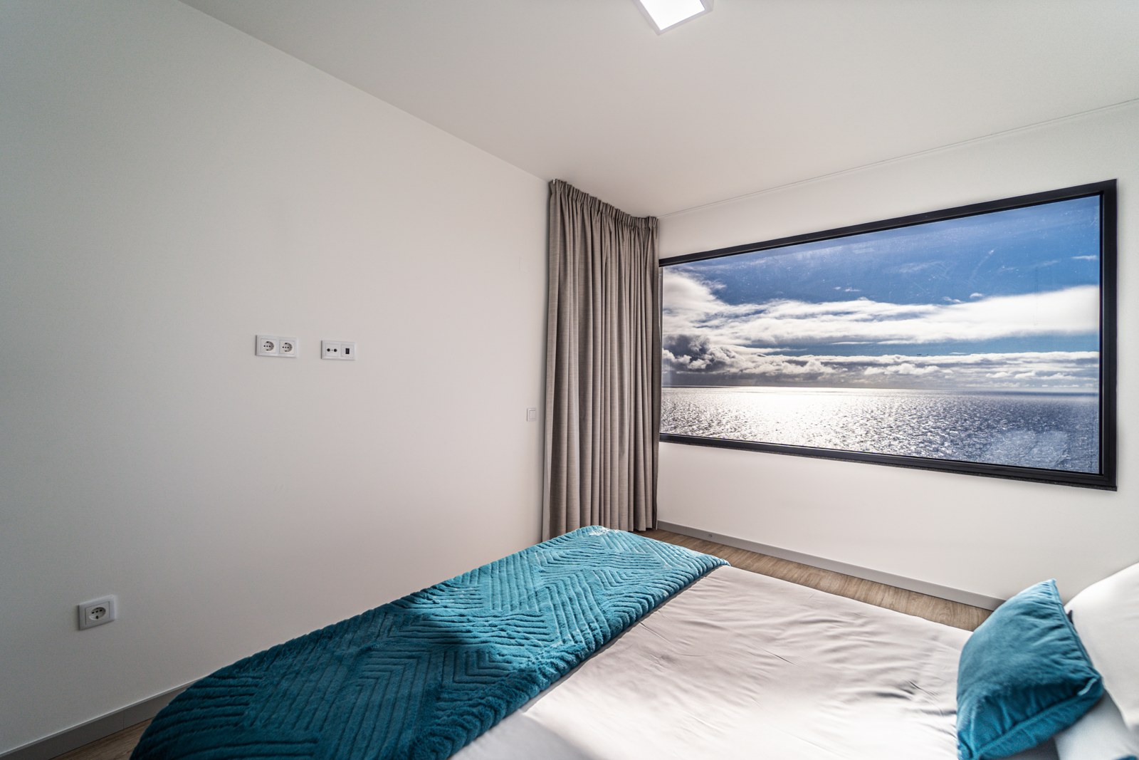 Bedroom with teal linens and a framed sea-view window at Guesthouse Olival, Madeira