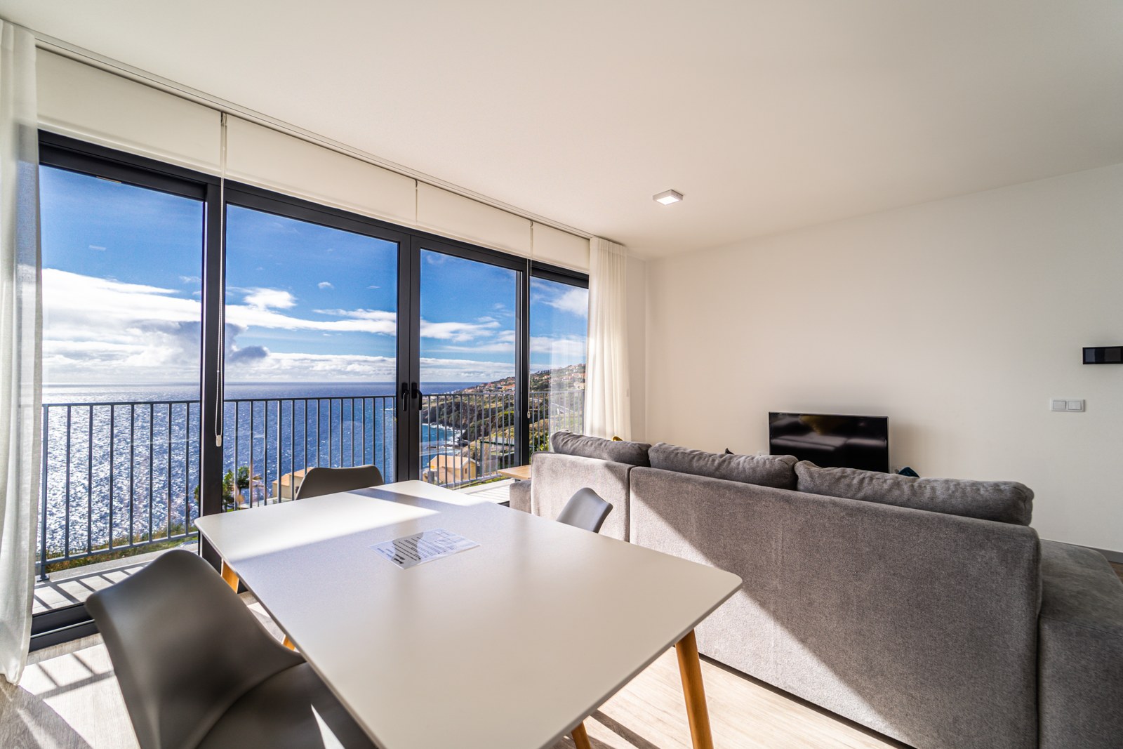 Living room with grey corner sofa and sliding doors to a sea-view balcony at Guesthouse Olival