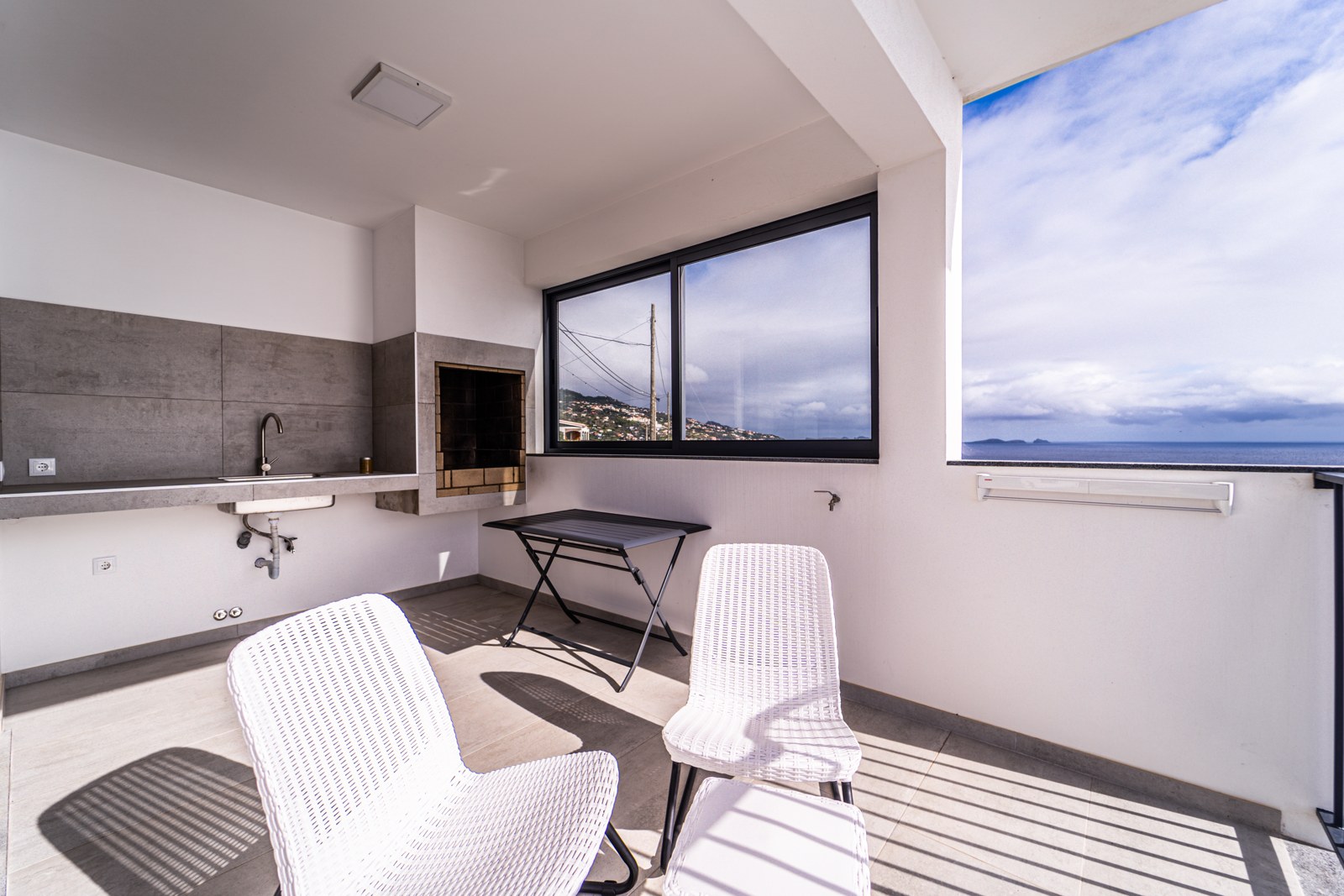Covered terrace with a built-in stone barbecue, sink and sea-view window at Guesthouse Olival