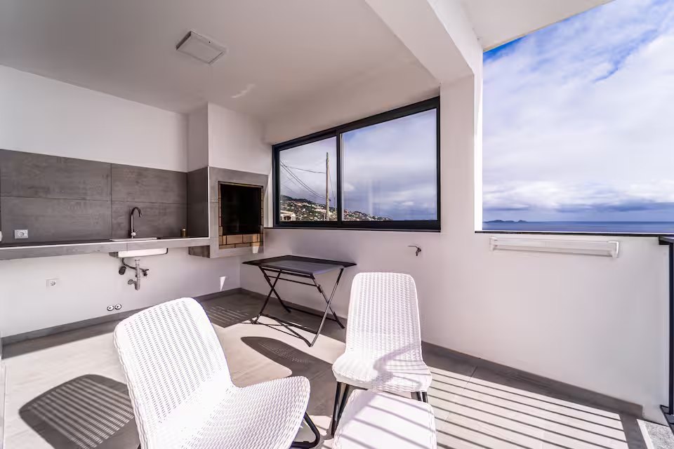 Shaded outdoor dining area beside the barbecue with ocean-view window at Guesthouse Olival