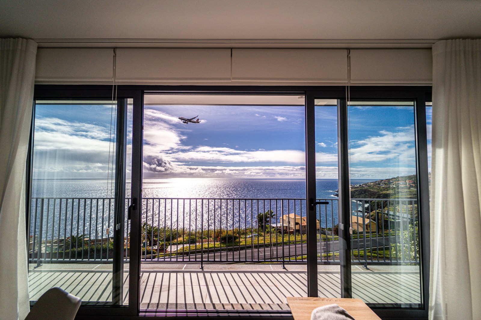 View through the living-room sliding doors to the balcony, ocean and an incoming plane at Guesthouse Olival, Madeira